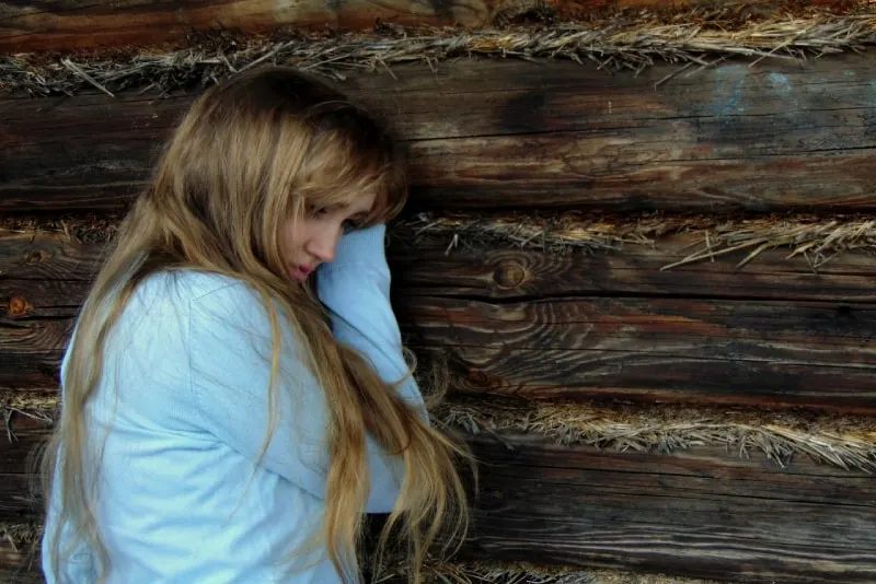 sad woman in white top leaning on wooden wall