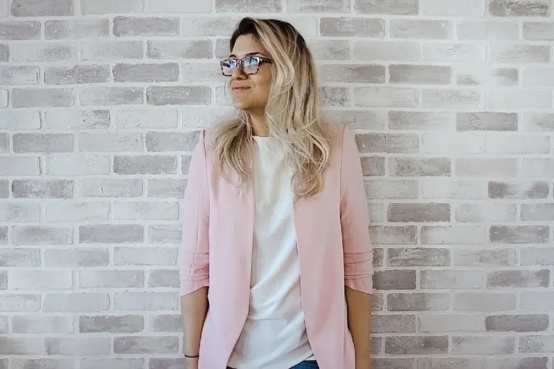 blonde woman in pink cardigan leaning on wall