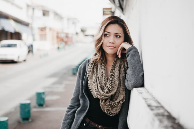 mujer con abrigo gris apoyada en una pared blanca