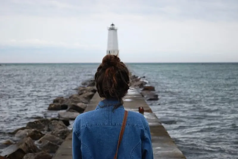 woman in denim shirt looking at lighthouse