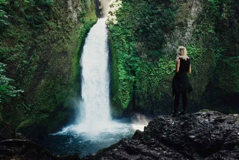 blonde woman in black top looking at waterfall
