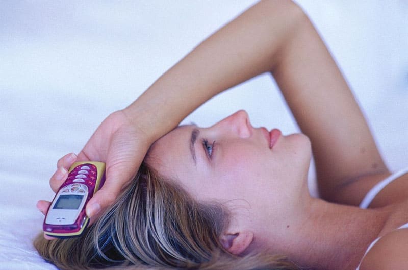 woman lying holding an old nokia cellphone with hand above her head