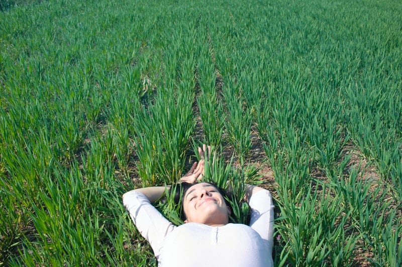 woman lying on green grasses smiling and closing her eyes