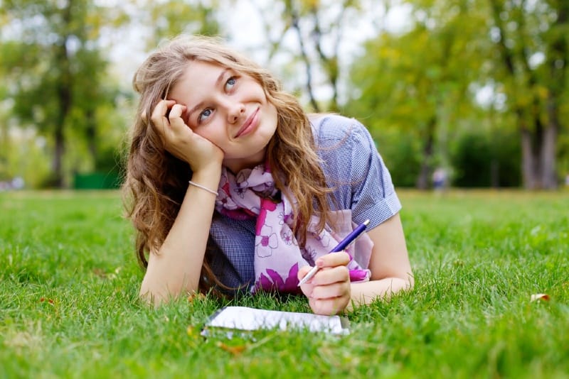mujer sosteniendo un bolígrafo tumbada en la hierba