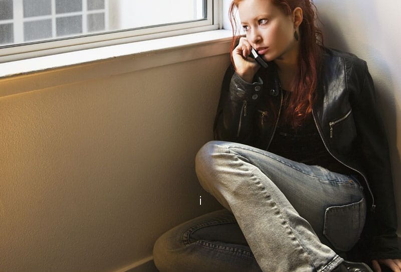 woman on the cellphone calling while sitting on the floor near the window