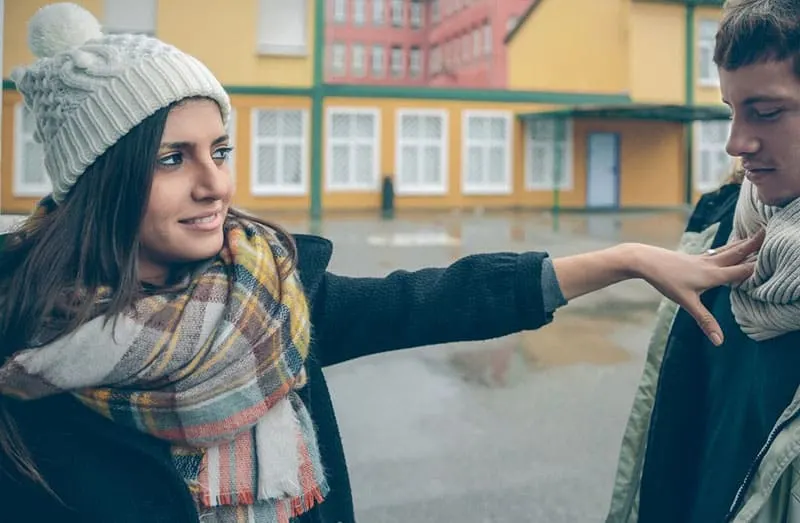 woman push a man standing outdoors wearing winter clothes