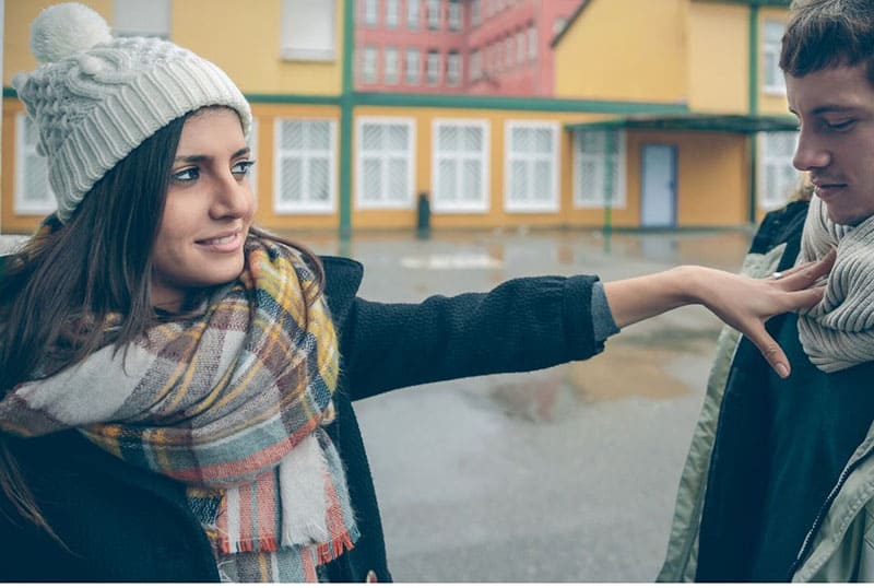 donna che spinge un uomo in piedi all'aperto indossando un abito invernale