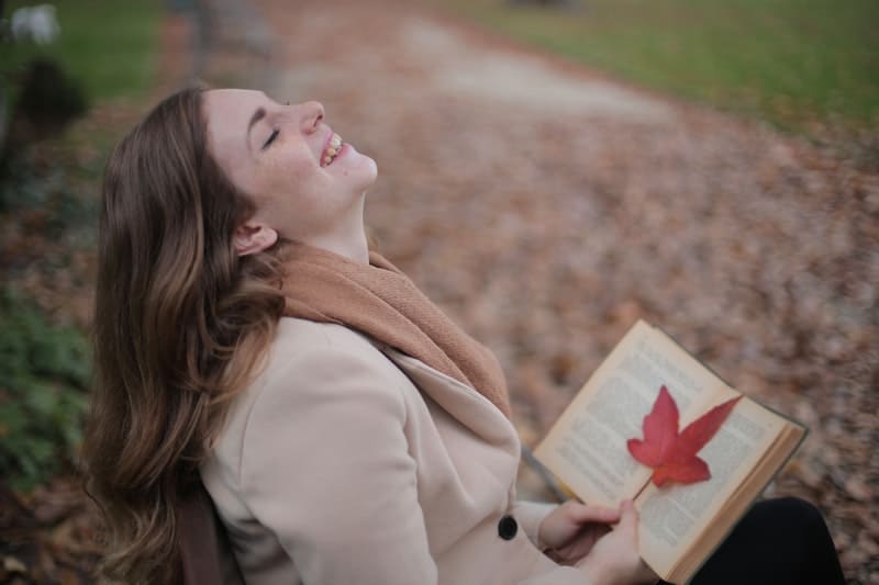 mulher a ler um livro ao ar livre enquanto se ri