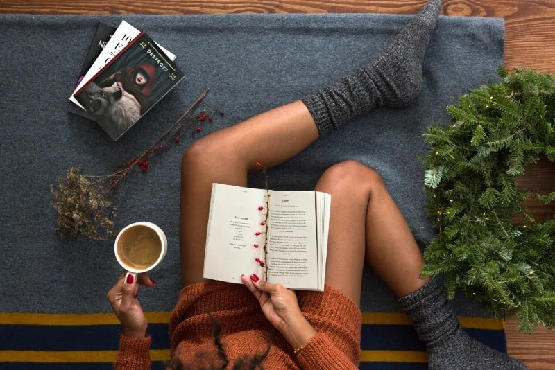 woman with gray socks reading book and holding white mug