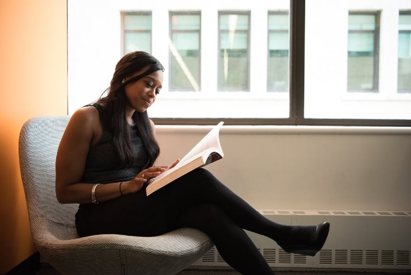 woman in black top reading book while sitting on chair