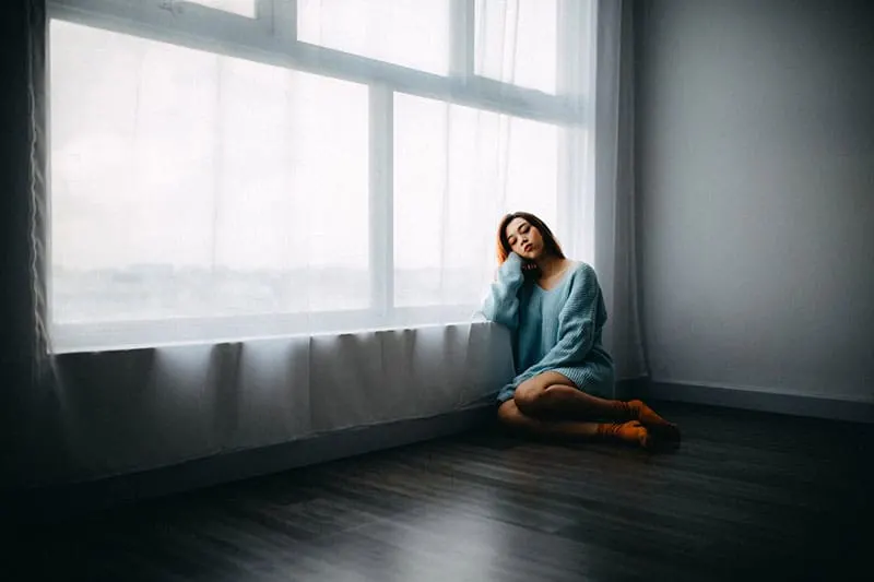 woman sad in in a large room sitting on the floor near the large windows