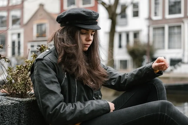 woman in black leather jacket sitting near city canal