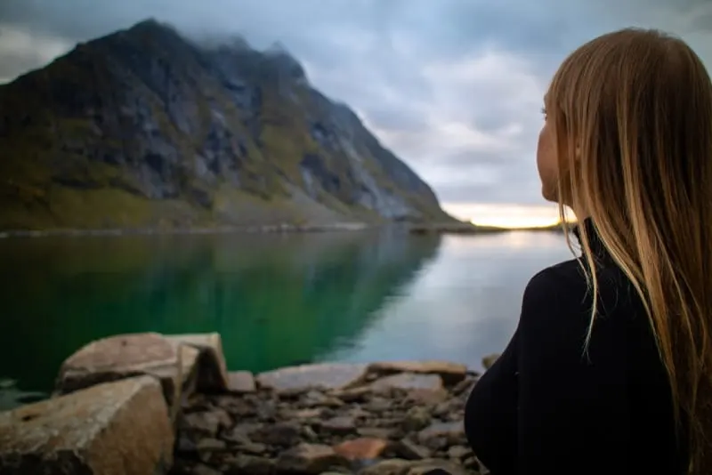 woman in black jacket sitting near lake