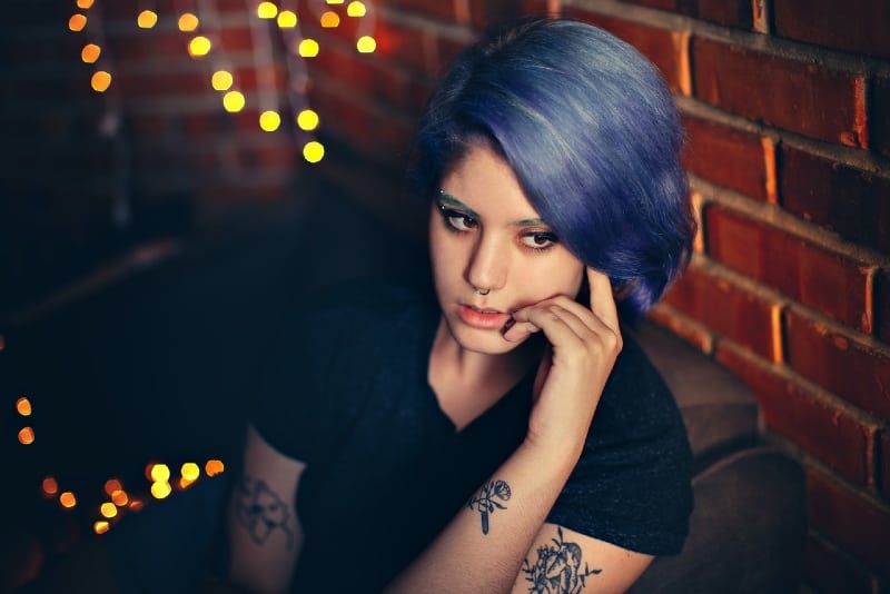 tattooed woman with blue hair sitting near wall