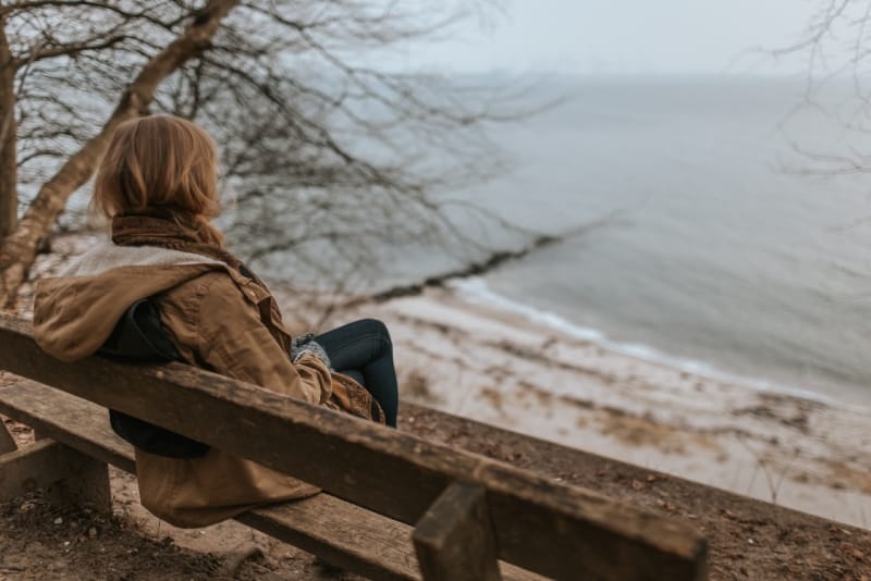 woman sitting on wooden bench looking at water