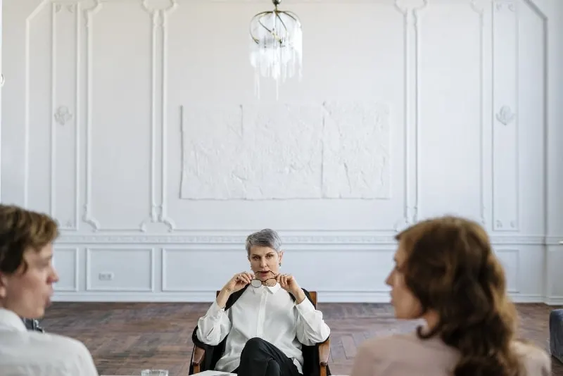 woman in white shirt sitting on chair listening to couple talking