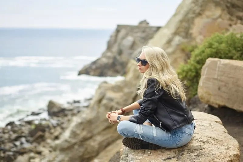 blonde woman with sunglasses sitting on cliff
