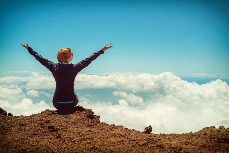 woman sitting on cliff raising up both hands