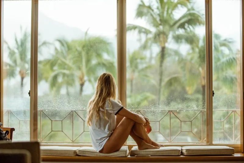 blonde woman sitting on white cushion looking through window