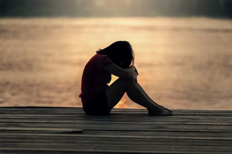 sad woman sitting on wooden dock near water
