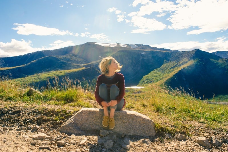 blonde woman sitting on rock near mountain