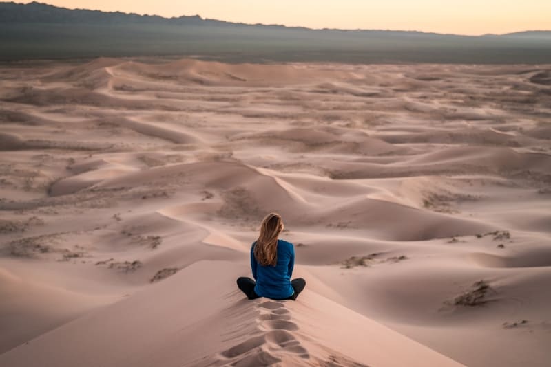 woman in blue top sitting on sand field