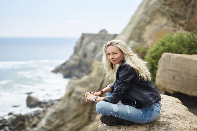 blonde woman in black jacket sitting on stone