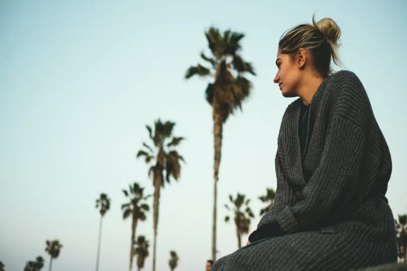 woman in gray sweater sitting near coconut trees outdoor
