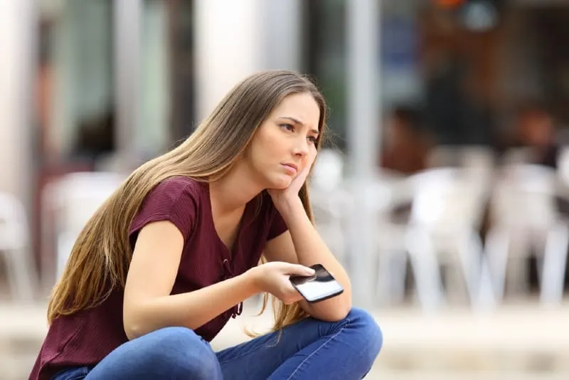 sad woman holding phone while sitting outdoor