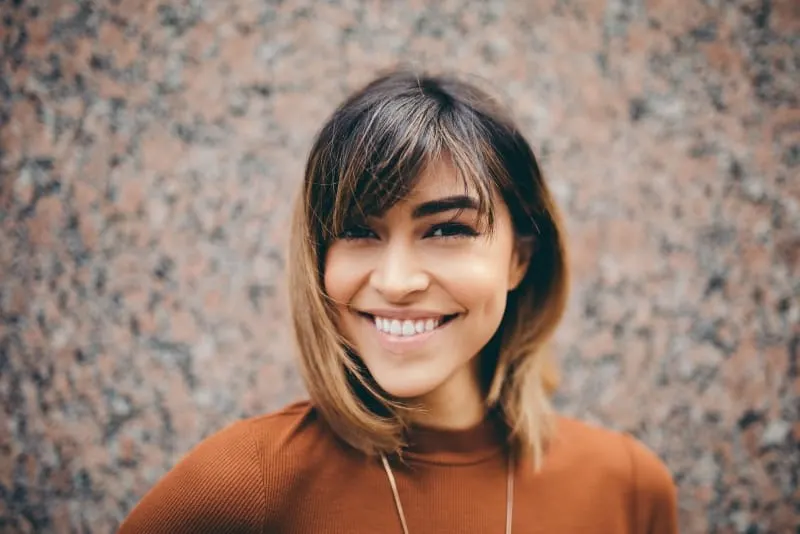 woman in brown shirt smiling near brown wall