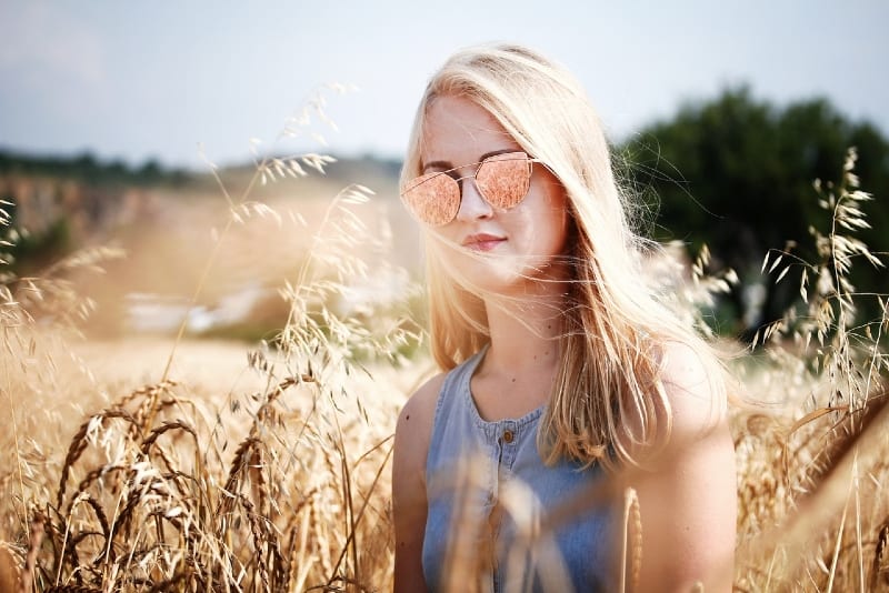 donna bionda con occhiali da sole in piedi in un campo di grano