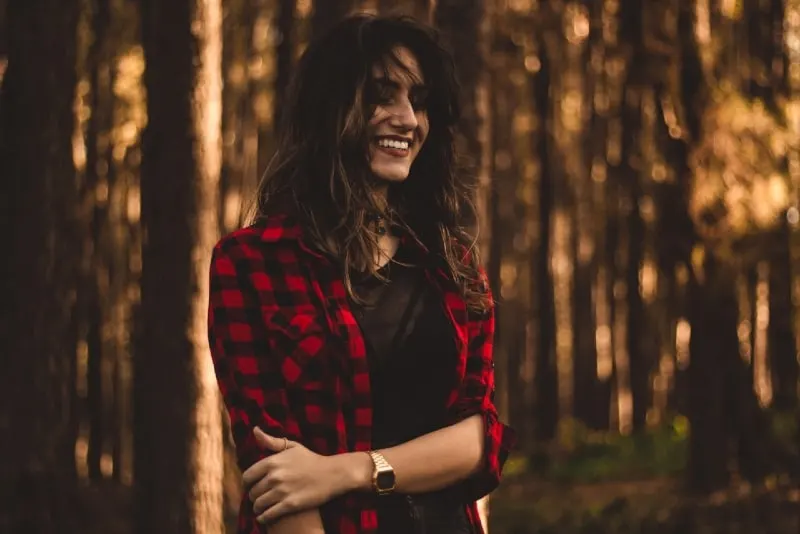 smiling woman in red checked shirt standing in forest