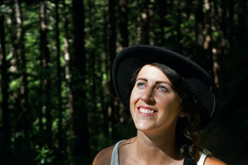 donna sorridente con cappello nero in piedi nella foresta