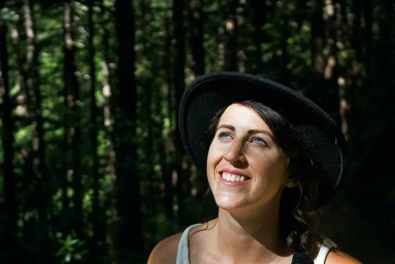 smiling woman with black hat standing in forest