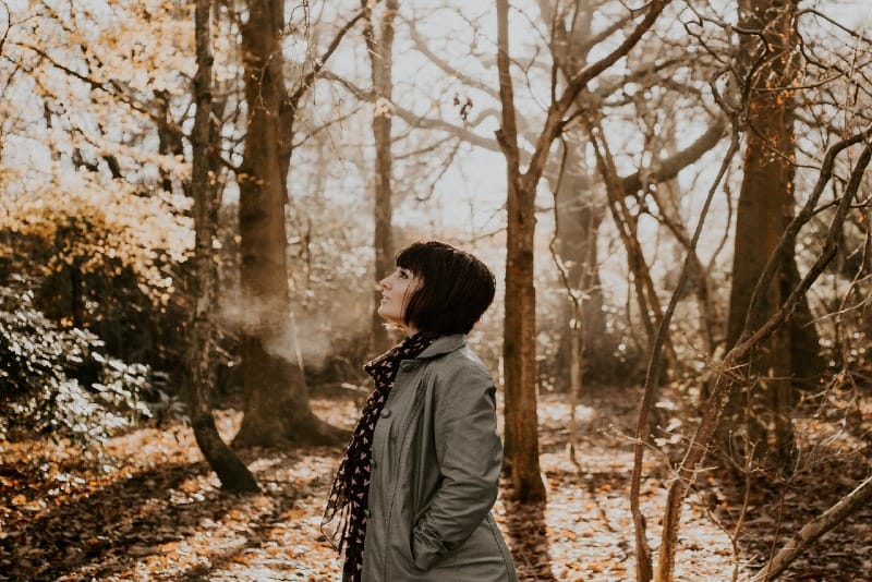 woman standing in woods looking up