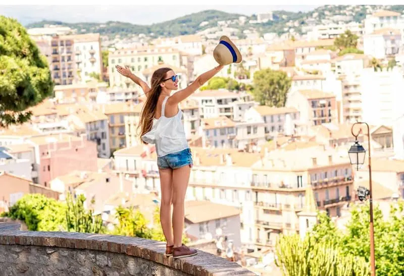 woman standing on a ledge of a building overlooking the city with arms raised for happiness