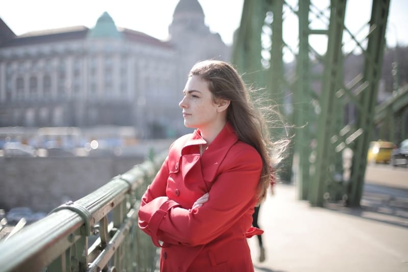 mujer con abrigo rojo de pie en el puente y pensando