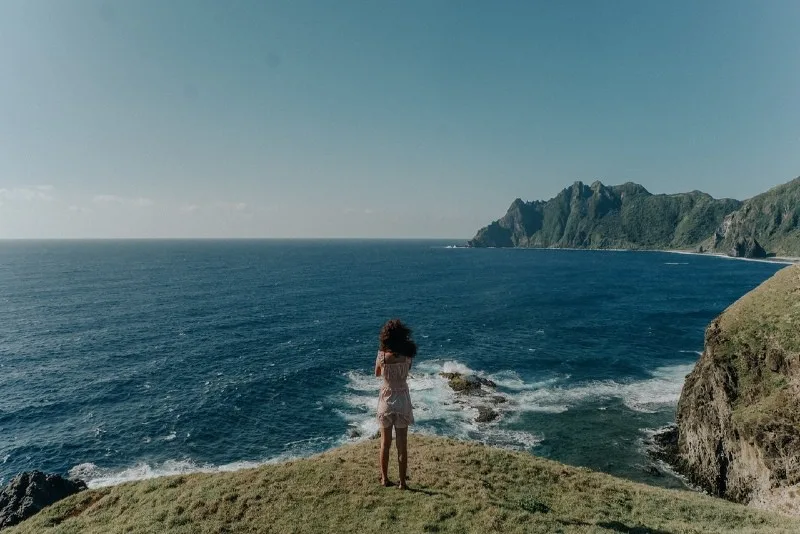 woman standing on cliff looking at sea