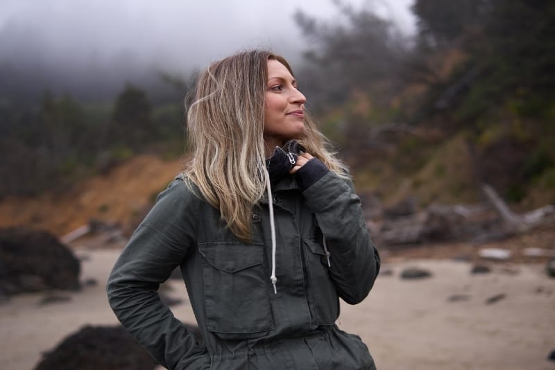 happy woman in gray jacket standing on seashore
