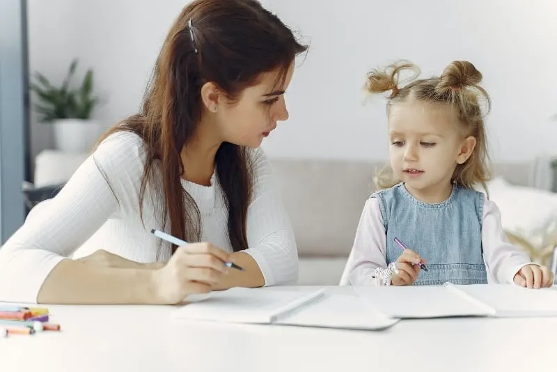 woman teaching child how to draw while sitting on floor
