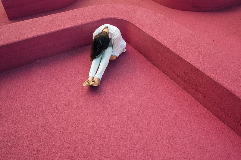 donna nascosta in un angolo di una struttura rosa che indossa un top bianco e jeans con la testa china