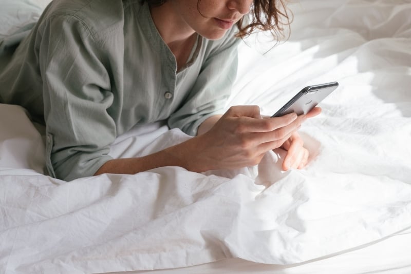 woman using smartphone while lying on bed