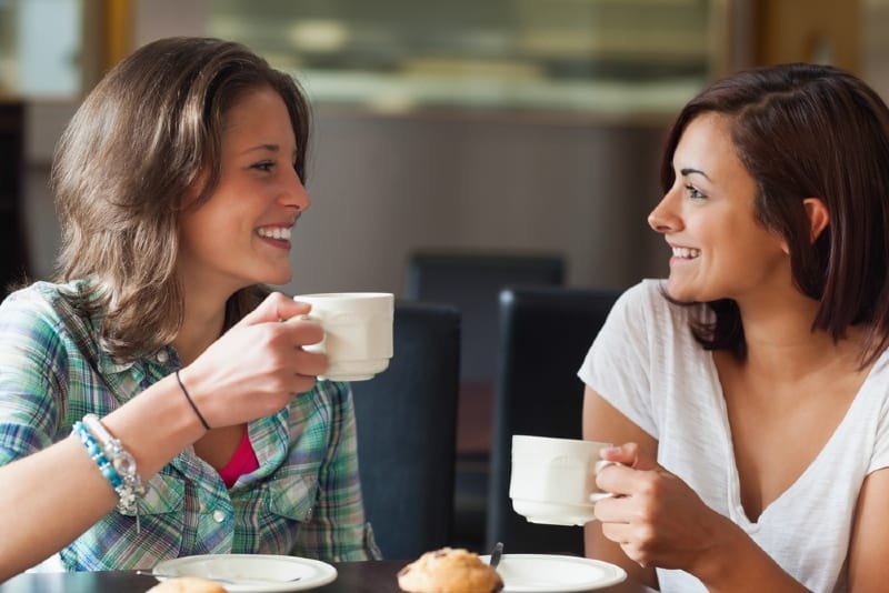 two women holding white mugs and talking