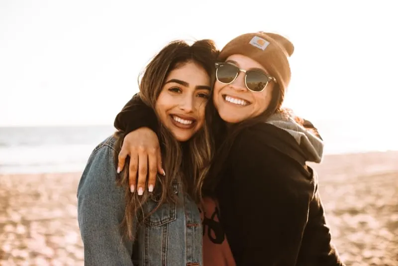 two smiling women hugging while standing on the beach