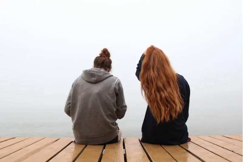 two women sitting on wooden dock and talking