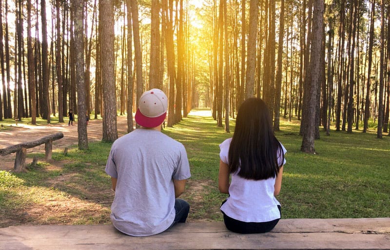 young couple sitting on a bench in the middle of the countryside woods