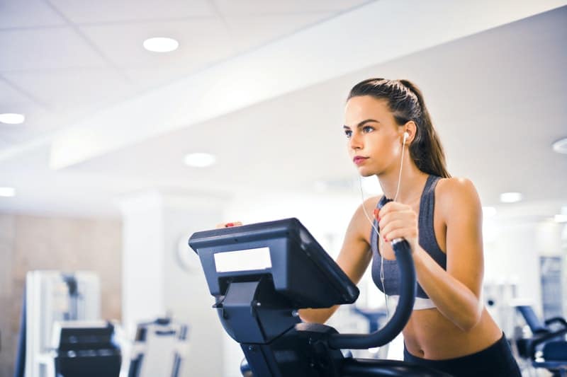 jovem mulher numa passadeira a fazer exercício, com roupa desportiva e auscultadores