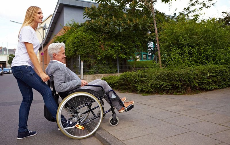 young woman helping a man in the wheelchair thru the curbstone