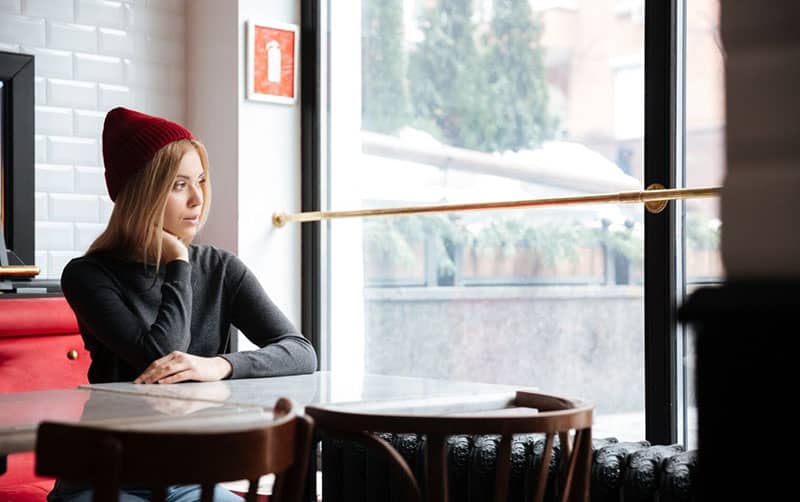 giovane donna con berretto rosso seduta all'interno di un caffè che guarda fuori