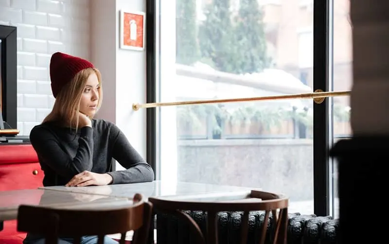 young woman in red cap sitting inside a cafe looking outside
